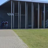 Un grupo de jóvenes camina hacia la entrada del Museo de la Constitución Nacional en Santa Fe, un edificio moderno de hormigón con columnas metálicas delgadas.