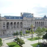 Fachada de la Casa de Gobierno de Santa Fe, un edificio histórico de estilo francés frente a una plaza con palmeras y árboles.