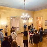 Un grupo de visitantes escucha a un guía en el salón principal del Club del Orden en Santa Fe, destacando sus paredes señoriales y una araña de luces.