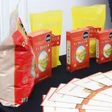 Mesa promocional con paquetes de cacao en polvo El Quillá, bolsas amarillas de la marca y folletos distribuidos para un evento turístico o cultural en Santa Fe.