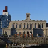 Fachada del Museo del Puerto de Santa Fe vista desde el agua, un edificio histórico gris con una torre de reloj central sobre un paredón de piedra.