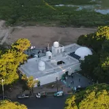 Vista aérea del observatorio CODE en la Costanera de Santa Fe, un edificio blanco con cúpulas astronómicas rodeado de árboles y la playa.