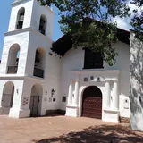 Fachada colonial blanca de la Iglesia y Convento de San Francisco en Santa Fe, con un portal de madera oscura y una torre campanario de tres niveles a la izquierda.